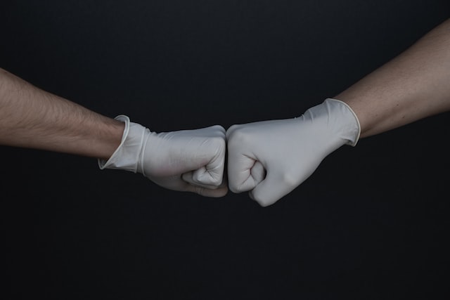 Zwei Personen mit weißen Latexhandschuhen berühren sich mit ihren Fäusten
